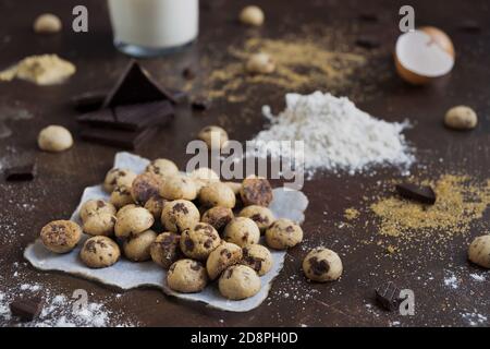 Shot of mini cookies on parchment paper with chocolate bars, flour, eggs, and milk on a table Stock Photo