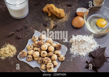 Top view of mini cookies on parchment paper with chocolate bars, flour, eggs, and milk on a table Stock Photo