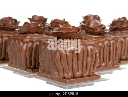 Square chocolate cake cupcakes on a chocolate candy bar frosted with choc frosting, handmade chocolate  rose on top, sitting on square clear plates is Stock Photo