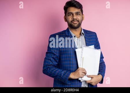 pleased successful man, financier, manager, dressed in formal wear, holding documentation, financial report, papers, smiling standing against pink bac Stock Photo