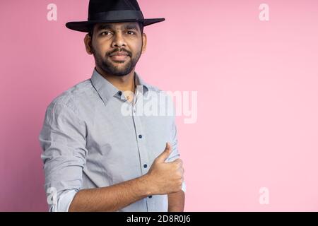 Thumbs up portrait of cheerful happy handsome young unshaven indian man wearing shirt, stylish black hat, looking at camera with broadly smile, standi Stock Photo