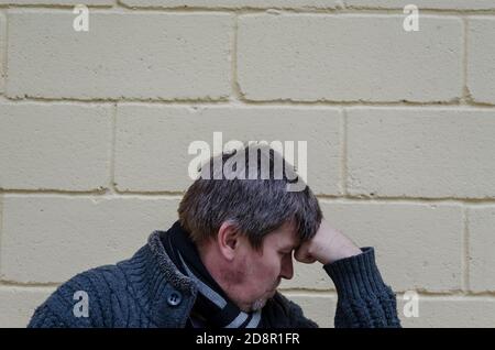 Portrait of man who put his head on his fist. A middle-aged grayish man is sitting in a thoughtful pose against a yellow wall background. Stock Photo