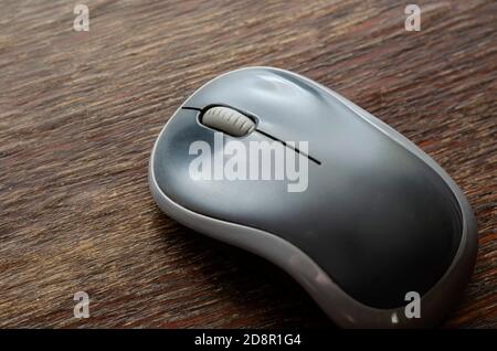 Close-up of a gray wireless computer mouse on a wooden surface. A device for controlling and operating a computer. Top view at an angle. Selective foc Stock Photo