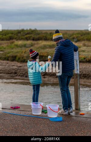 a father and young daughter crabbing on the sea wall at wells next the sea in norfolk on a rainy day. Stock Photo