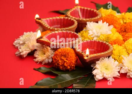 Flower Rangoli for Diwali or Pongal Festival made using Marigold or Zendu flowers and Clay Oil Lamp over redbackground. copy space. light at left side Stock Photo