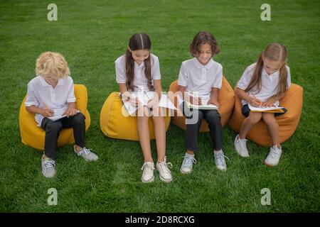 Pupils sitting on bag chairs and making notes Stock Photo