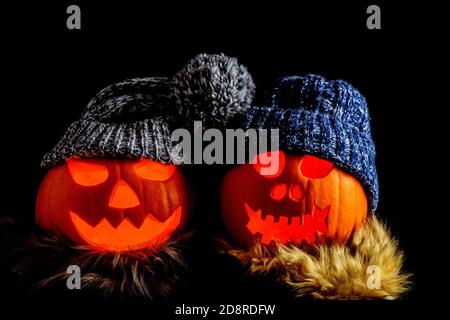 Two carved halloween pumpkins with knitted hats and scarves isolated on a black background Stock Photo