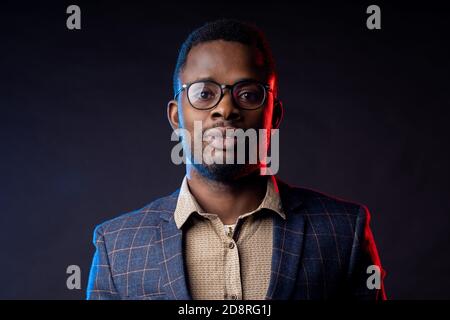 Closeup portrait of young handsome confident serious bearded african businessman in glasses, wearing shirt, checked suit, looking at camera, standing Stock Photo