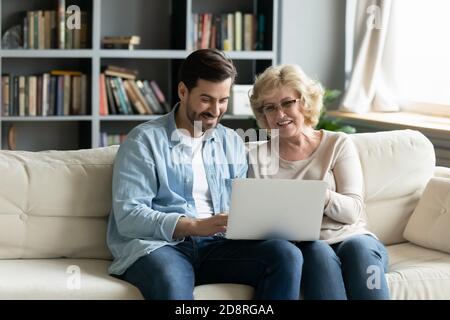Smiling young man teaching elderly senior mother using computer applications, Stock Photo