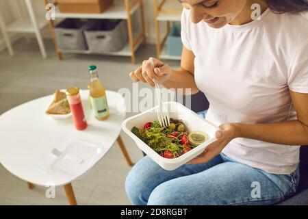 Happy young woman having lunch at home and eating veggie salad from plastic container Stock Photo