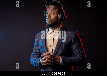 Closeup shot of african american young unshaven man listening music in headphones, looking down, posing in dark. Portrait of stylish DJ with headset, Stock Photo