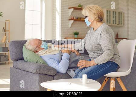 Senior wife taking care of her sick husband lying on sofa suffering from flu or common cold Stock Photo