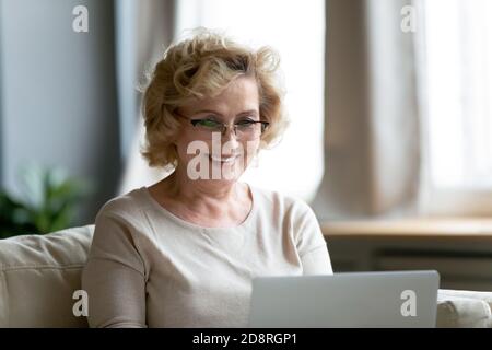 Pleased happy middle aged mature woman looking at computer screen. Stock Photo
