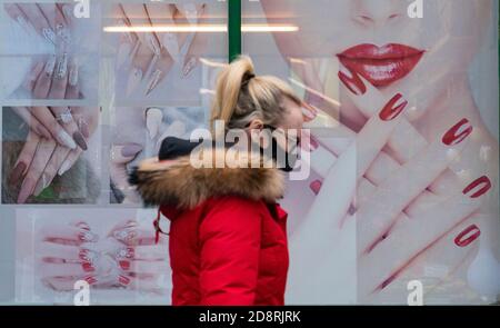 Woman wearing facemask walks past shop window of nail bar in Airdrie town centre during coronavirus pandemic, Scotland Uk Stock Photo