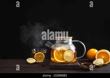 Citrus tea with  lemon, oranges  in modern glass teapot on dark wooden table, copy space. Fruit tea. Seasonal winter autumn hot drink. Stock Photo
