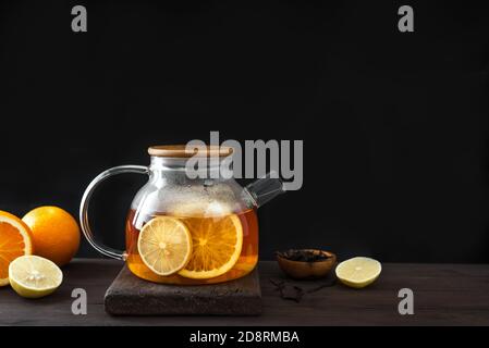 Citrus tea with  lemon, oranges  in modern glass teapot on dark wooden table, copy space. Fruit tea. Seasonal winter autumn hot drink. Stock Photo