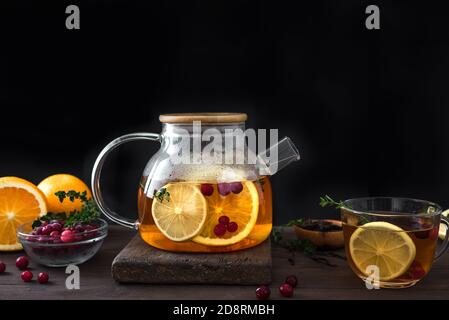 Citrus and berry tea with cranberries, lemon, oranges and thyme in a glass teapot on dark wooden table, copy space. Fruit tea. Seasonal winter autumn Stock Photo