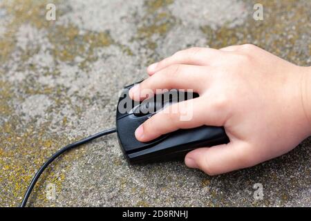 Little childs hand on a computer mouse, closeup. Child pressing a button holding a black pc mouse up close, top view. Young children on the internet Stock Photo