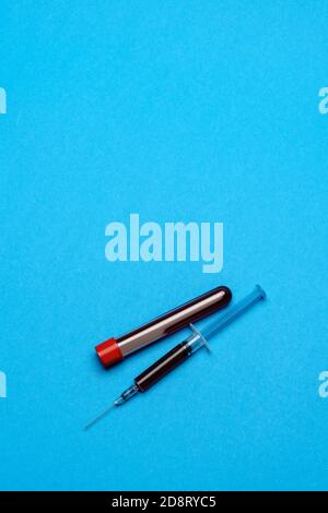 Syringe And Plastic Test Tube With Blood Sample over blue background with copyspace Stock Photo