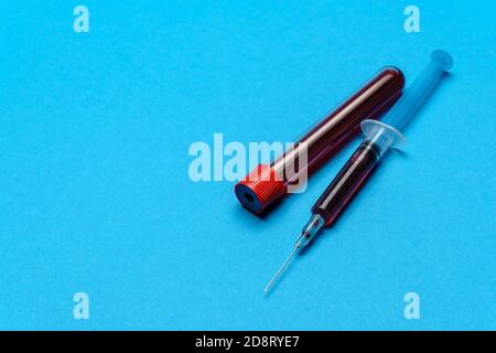 Syringe And Plastic Test Tube With Blood Sample over blue background with copyspace Stock Photo