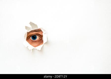 The human eye is watching us through a hole in a paper. Copy-space. Stock Photo
