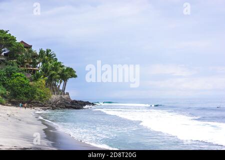 Beautiful beach in Indonesia with green palm trees and resort on the cliff, cloudy weather in the sea, travel vacation concept, Lombok Island Stock Photo