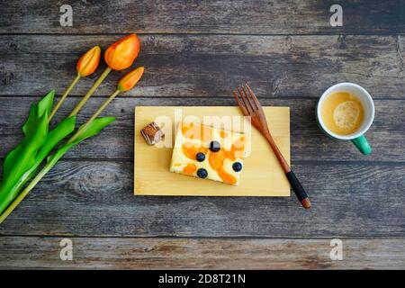 Coffee time in Germany: Home-baked cheese cake with a chocolate and coffee on a wooden background with orange tulip flowers for decoration. Stock Photo