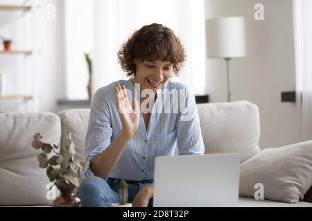 Close up smiling woman waving hand, using laptop at home Stock Photo