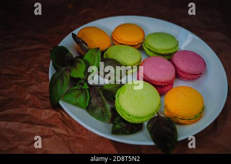 Colorful macaroons with basil leaves on a white plate. Close up macaron dessert pastel tones Stock Photo