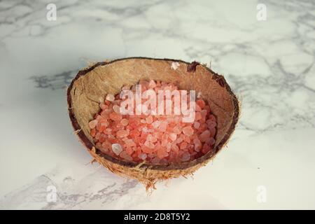 Coarse Pink Himalayan salt in a coconut shell with white and gray marble background Stock Photo