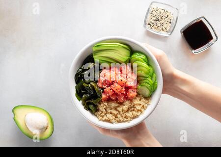woman's hands holding salmon fish poke bowl with avocado, quinoa, wakame Stock Photo