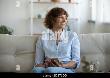 Close up overjoyed young woman holding phone, looking to aside Stock Photo