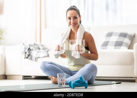 Motivated young woman works out at home on a mat in her fitness clothes. Stock Photo
