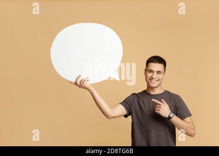 Smiling young guy with smart watch holds blank space for words in hand and points to abstract bubble Stock Photo