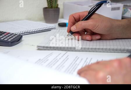 The student solves mathematical formulas. Man writes with a pen in a notebook. Homework. Notes in a notebook. Stock Photo