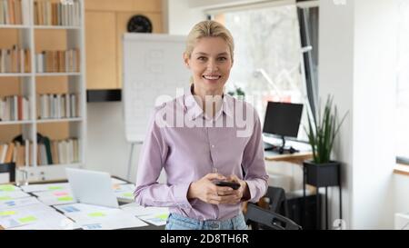 Portrait of smiling young european businesswoman with phone in hands. Stock Photo