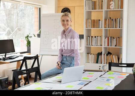 Confident smiling young blonde businesswoman leaning on table. Stock Photo