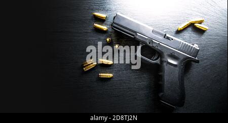 Detail on hand gun on black table banner or panorama photo on dark stone table top view. Gun shop with ammunition. 9 mm pistol gun weapon and bullets. Stock Photo