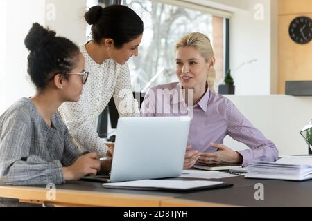 Focused happy millennial mixed race female employees discussing project. Stock Photo