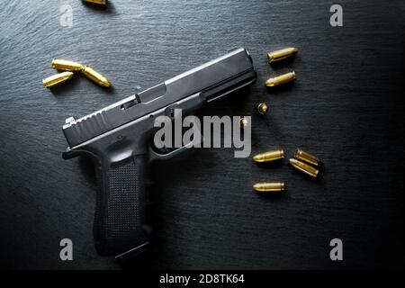 Top view of hand gun on black background with bullets around. 9mm pistol with ammunition on dark table.  Stock Photo