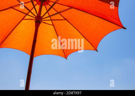 Orange color beach umbrella made of wooden for protected sunlight with a bright blue sky background. Stock Photo