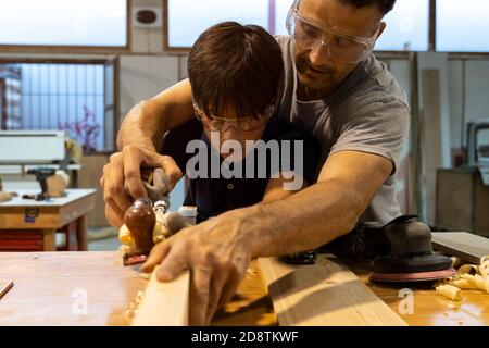 Father teaching son carpentry and sanding wood. Selective focus Stock Photo