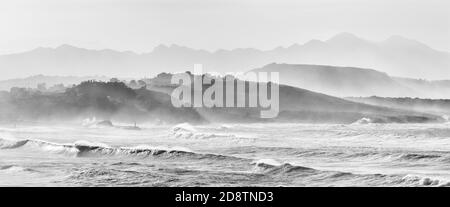 A mountain landscape in silhouette with beach and waves breaking in the foreground Stock Photo
