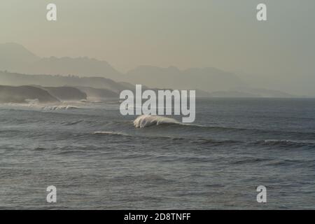 A mountain landscape in silhouette with beach and waves breaking in the foreground Stock Photo