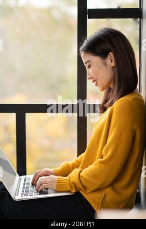 Asian woman working on laptop at home or in cafe on window. Stock Photo
