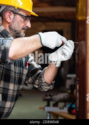 Carpenter worker at work with screwdriver, repairs and installs the door frame of a room. Construction industry. Carpentry. Stock Photo