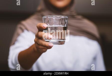 Unrecognizable Muslim Woman Offering Glass Of Water To Camera Indoors Stock Photo