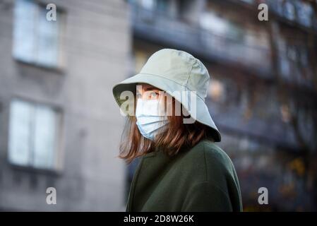 RIGA, LATVIA. 28th October 2020. Young woman wearing face protective mask and hat at bus stop. Stock Photo