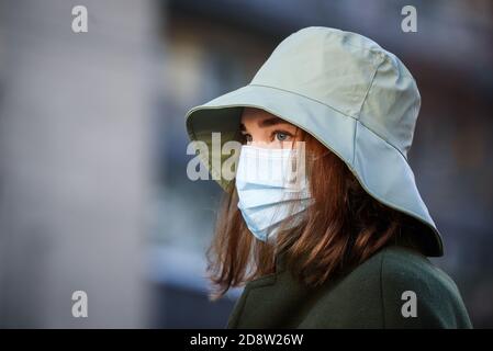 RIGA, LATVIA. 28th October 2020. Young woman wearing face protective mask and hat at bus stop. Stock Photo