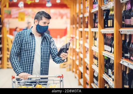 Young man with protective face mask shopping red wine from supermarket during coronavirus reopening outbreak Stock Photo